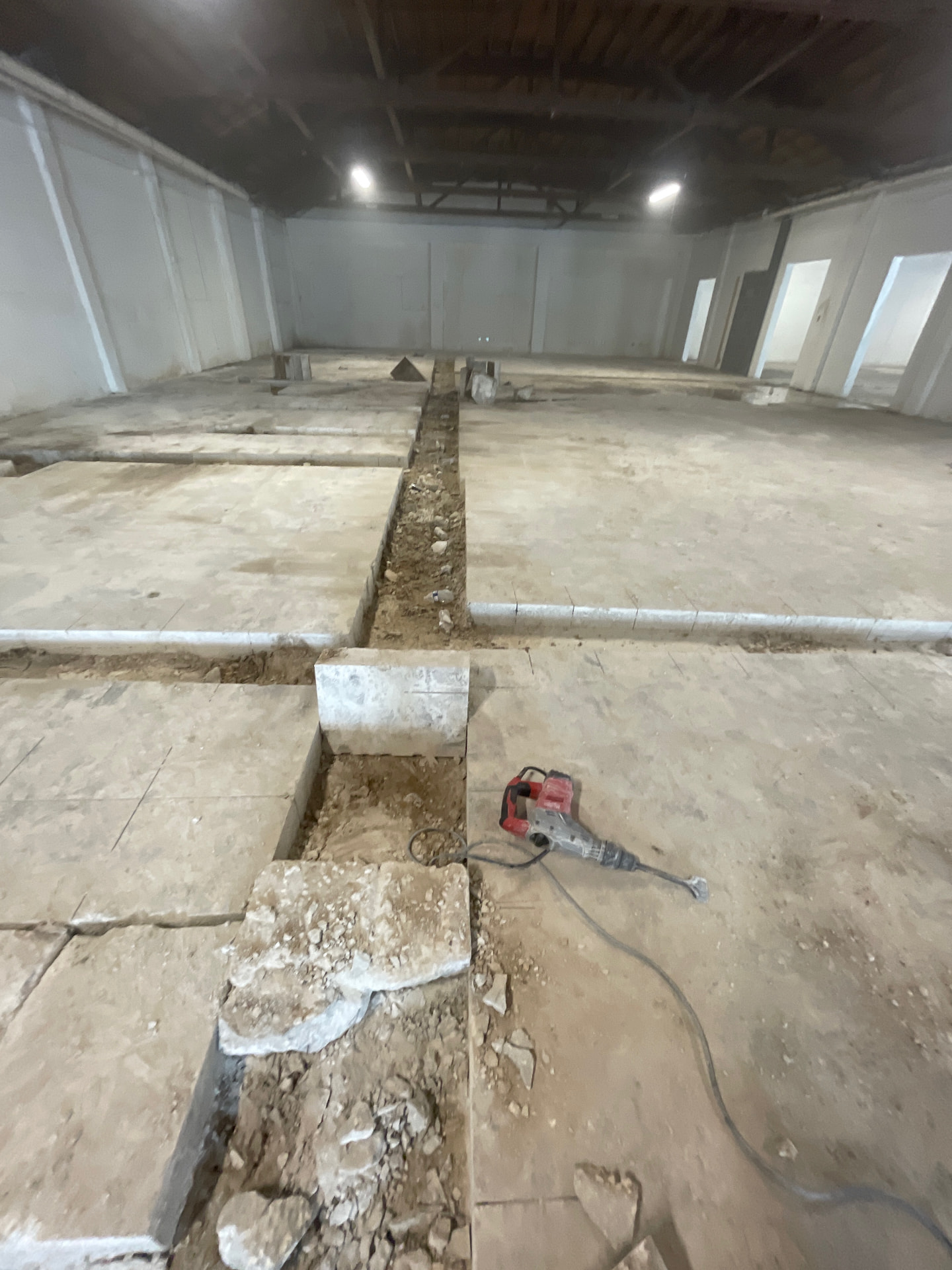 Interior concrete slab cut into sections with a trench and a red demolition hammer